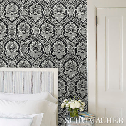 Black-and-white damask wallpaper behind a white striped headboard bed with white bedding and a vase of white flowers.
