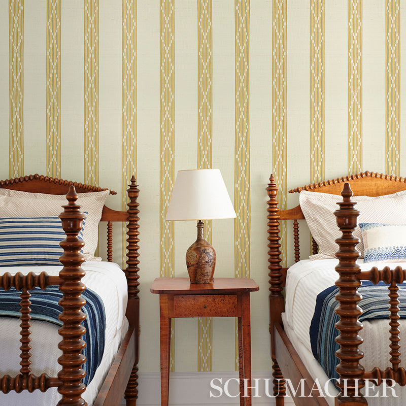 Twin carved wooden beds with blue striped bedding and a wooden nightstand with a ceramic lamp against yellow wallpaper.