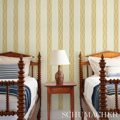 Two antique carved wooden twin beds with blue striped bedding, central nightstand and lamp, yellow striped wallpaper.