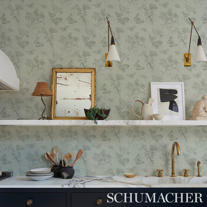 Kitchen scene with butterfly linen black wallpaper, marble countertop, brass faucet, blue cabinetry, framed art, and kitchen utensils.