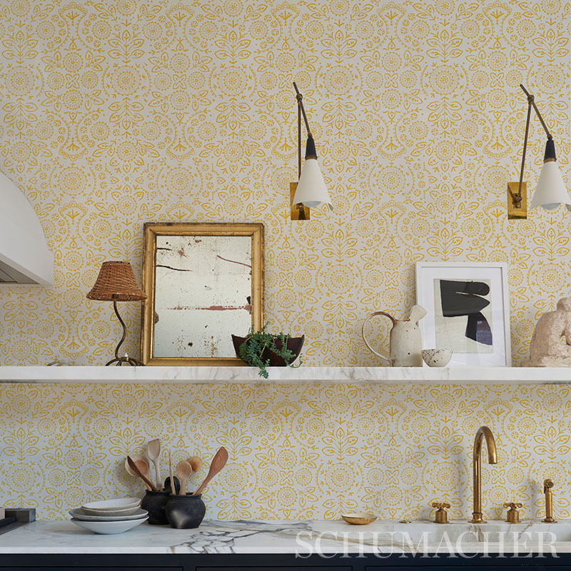 Yellow damask wallpaper with a white shelf, framed art, plants and brass kitchen faucet accents.