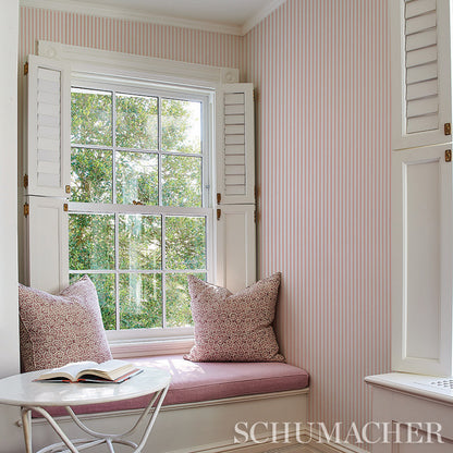 Cozy cottage reading nook with navy striped wallpaper, white window shutters, pink cushions, and a round white table with an open book.