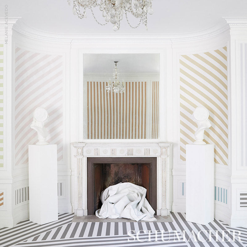 Elegant white ornate fireplace with pastel striped walls, busts on pedestals, chandelier, and fabric draped in the hearth.