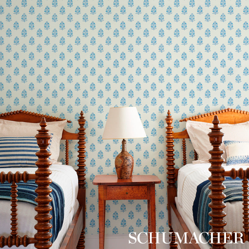 Two carved-wood four-poster twin beds with blue bedding, a wooden nightstand and ceramic lamp, blue floral wallpaper.