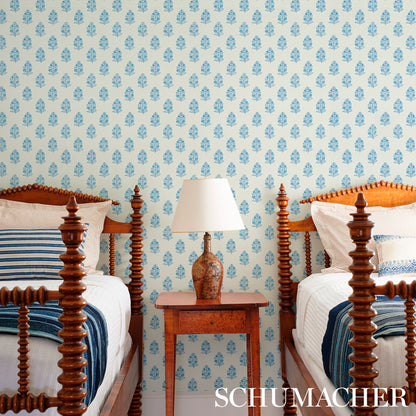 Two carved-wood four-poster twin beds with blue bedding, a wooden nightstand and ceramic lamp, blue floral wallpaper.