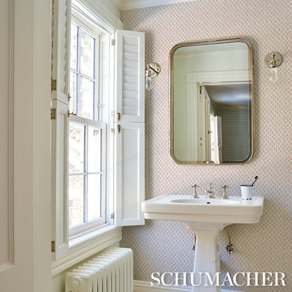 White pedestal sink with chrome taps and rounded mirror, pink dotted wallpaper, window with shutters, radiator beneath.
