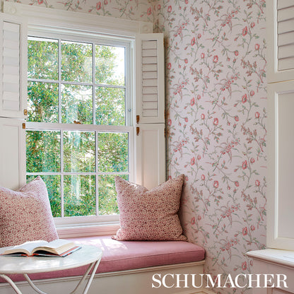 Pink cushioned window nook with white shutters, floral wallpaper, two pink patterned pillows, open book on round white table.