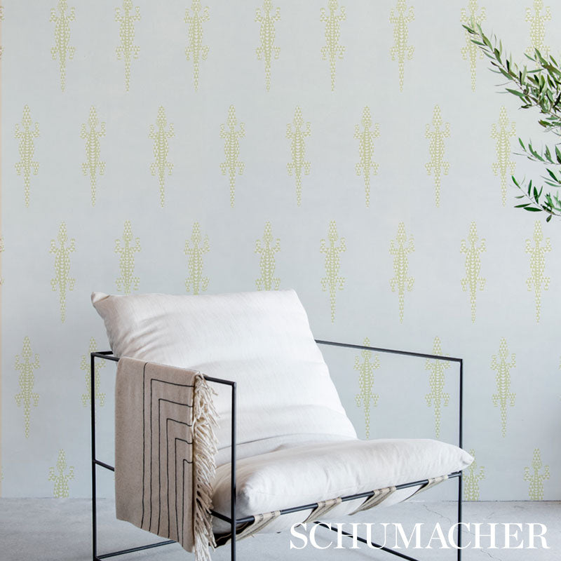 Minimalist black metal-frame lounge chair with white cushion and beige tassel throw; pale patterned wallpaper and greenery.