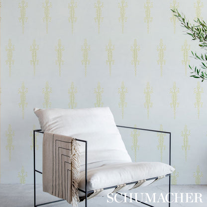 Minimalist black metal-frame lounge chair with white cushion and beige tassel throw; pale patterned wallpaper and greenery.