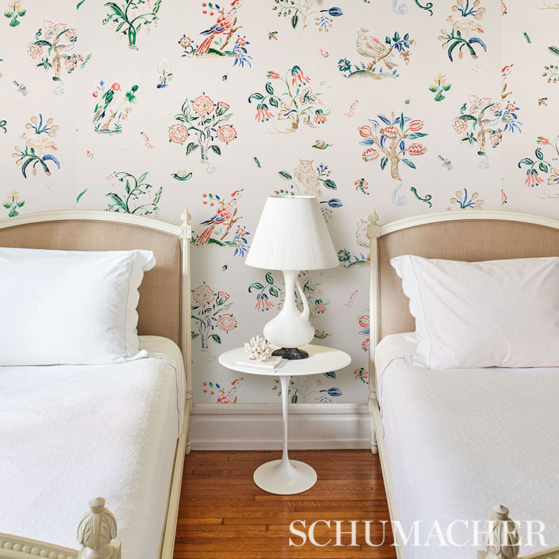 Twin beds with white bedding and beige headboards, white round nightstand and lamp, colorful floral wallpaper backdrop.