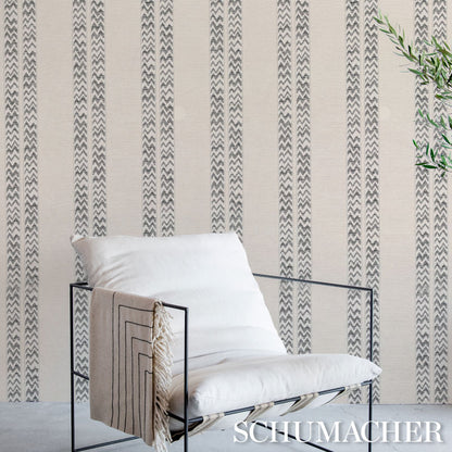 Black metal-framed lounge chair with white cushions and beige throw, against striped chevron wallpaper.
