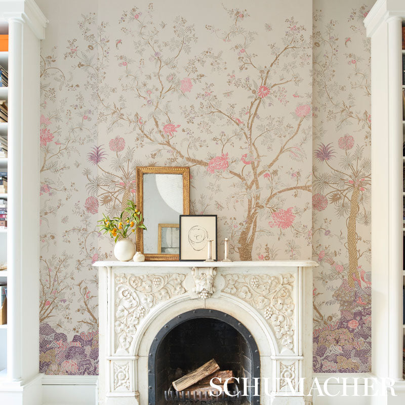 Ornate white carved fireplace with arched opening, pale pink floral wallpaper; mantel with frames, vase and candle.
