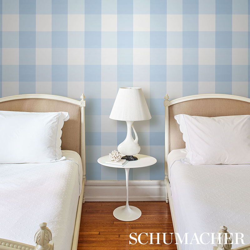 Twin bedroom with light beige headboards, white bedding, white round side table and lamp, blue plaid wallpaper, wooden floor.