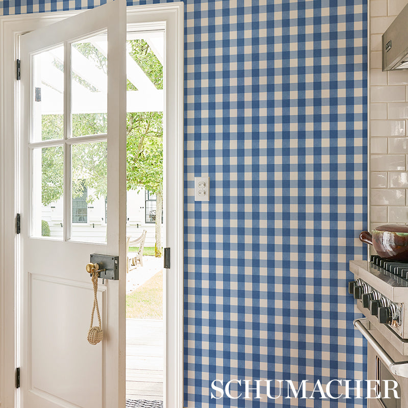 Blue and white gingham wallpaper in kitchen, white door with glass panes opened to sunny outdoor patio; stove on right.