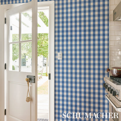 Blue and white gingham wallpaper in kitchen, white door with glass panes opened to sunny outdoor patio; stove on right.