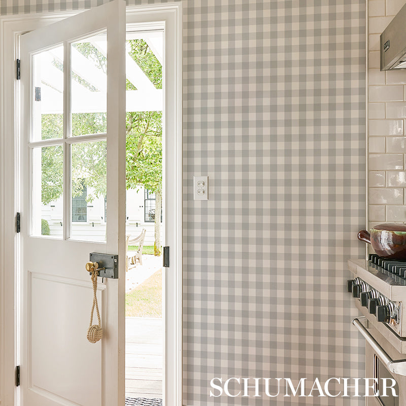 Bright interior with gray plaid wallpaper on the walls; white door with glass, brass rope pull, white subway tile, stainless stove.