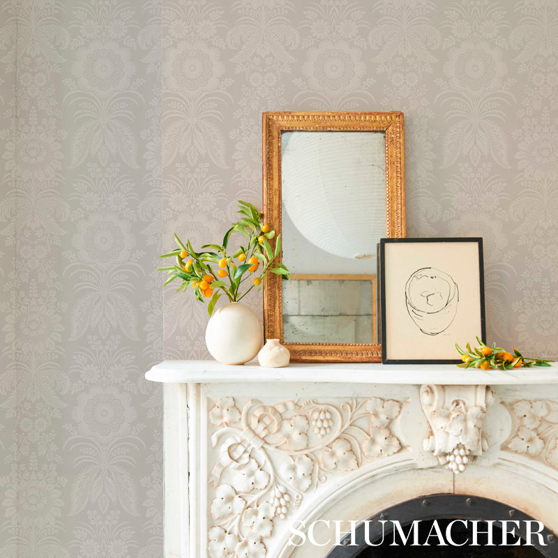 Ornate white fireplace mantel with floral carving, gold-framed mirror, black-framed sketch, and vase of orange blossoms.