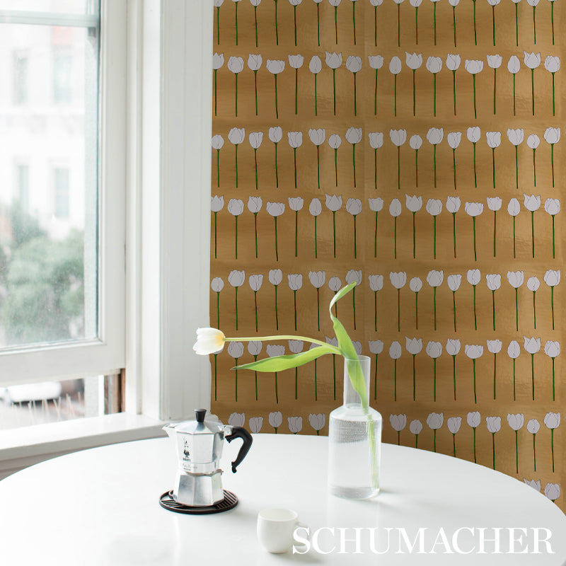 Round white table by a window; glass bottle with a white tulip, moka pot, and white cup; brown floral wallpaper backdrop.