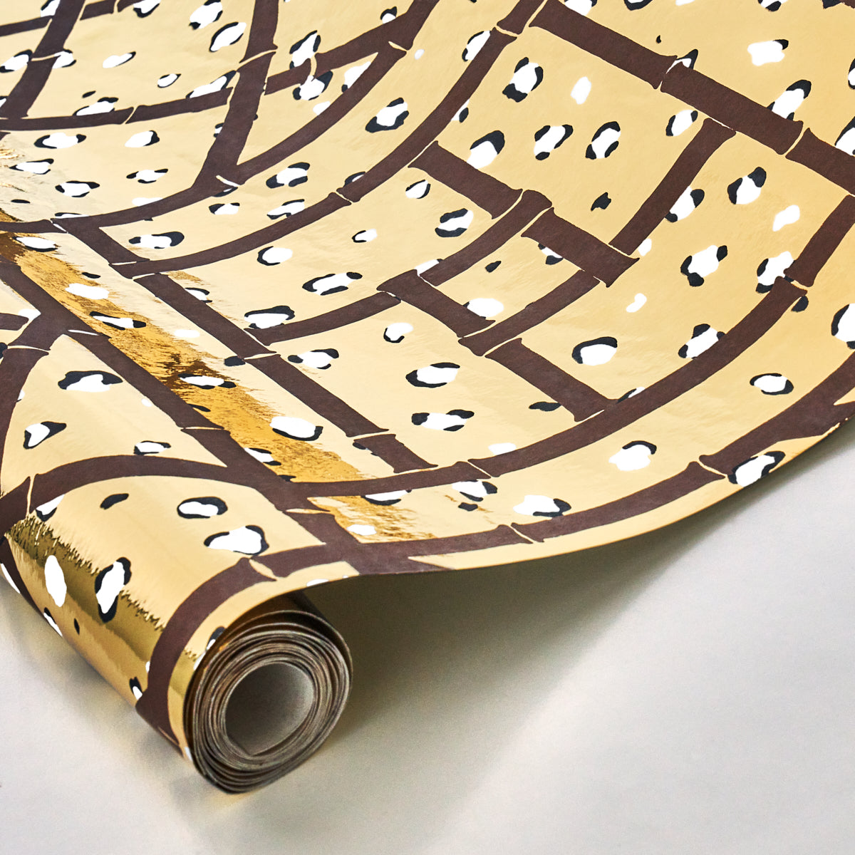 Decorative wallpaper roll with tan background, brown curved lines, white dots and gold accents.