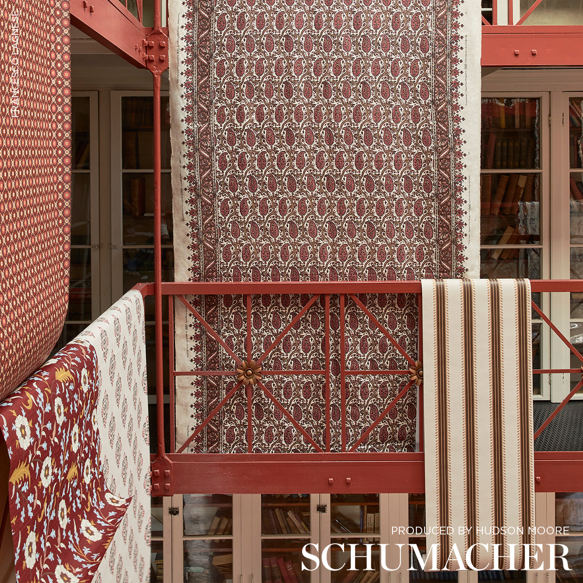 Maroon damask-pattern rug with cream border, vertically hung on red railing in a showroom.