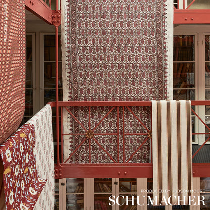 Maroon damask-pattern rug with cream border, vertically hung on red railing in a showroom.