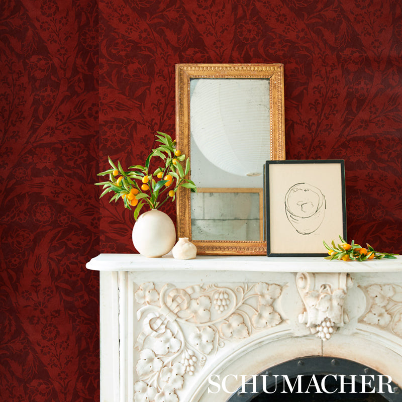 Ornate white carved mantel with gold mirror frame, black-framed sketch, round vase with yellow flowers, red damask wallpaper.