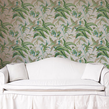 White upholstered sofa with two square cushions against tropical fern-pattern wallpaper.