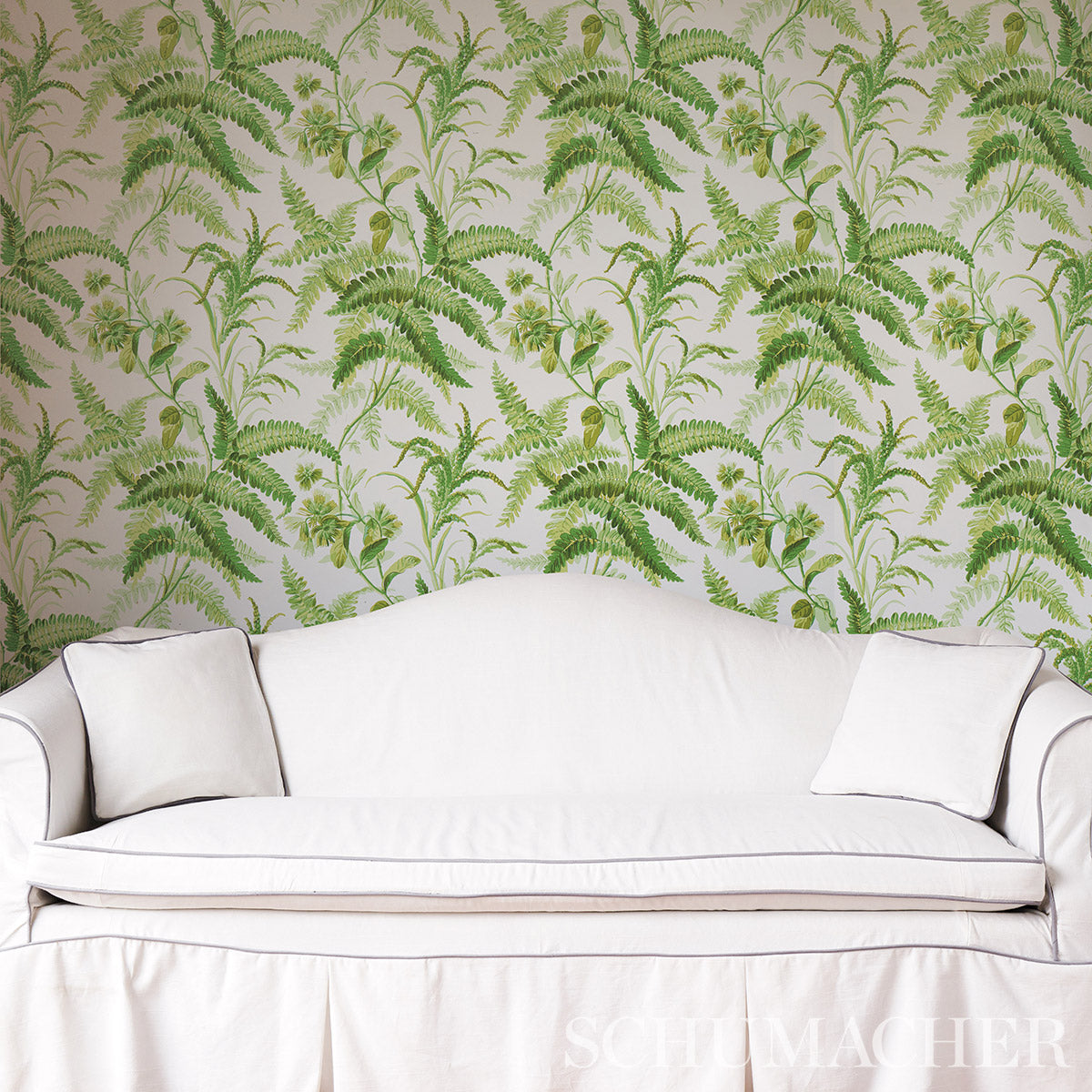 Cream linen-like sofa with curved arms and two white cushions against green fern-pattern wallpaper.