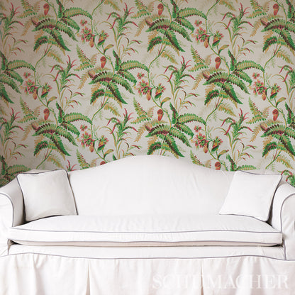 Cream sofa with two white cushions against tropical fern wallpaper with pink flowers.