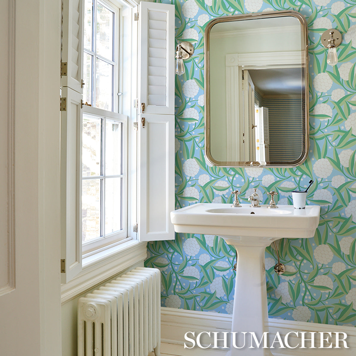 Vintage bathroom with white pedestal sink, brass faucet, pineapple-pattern teal wallpaper, gold-framed mirror.