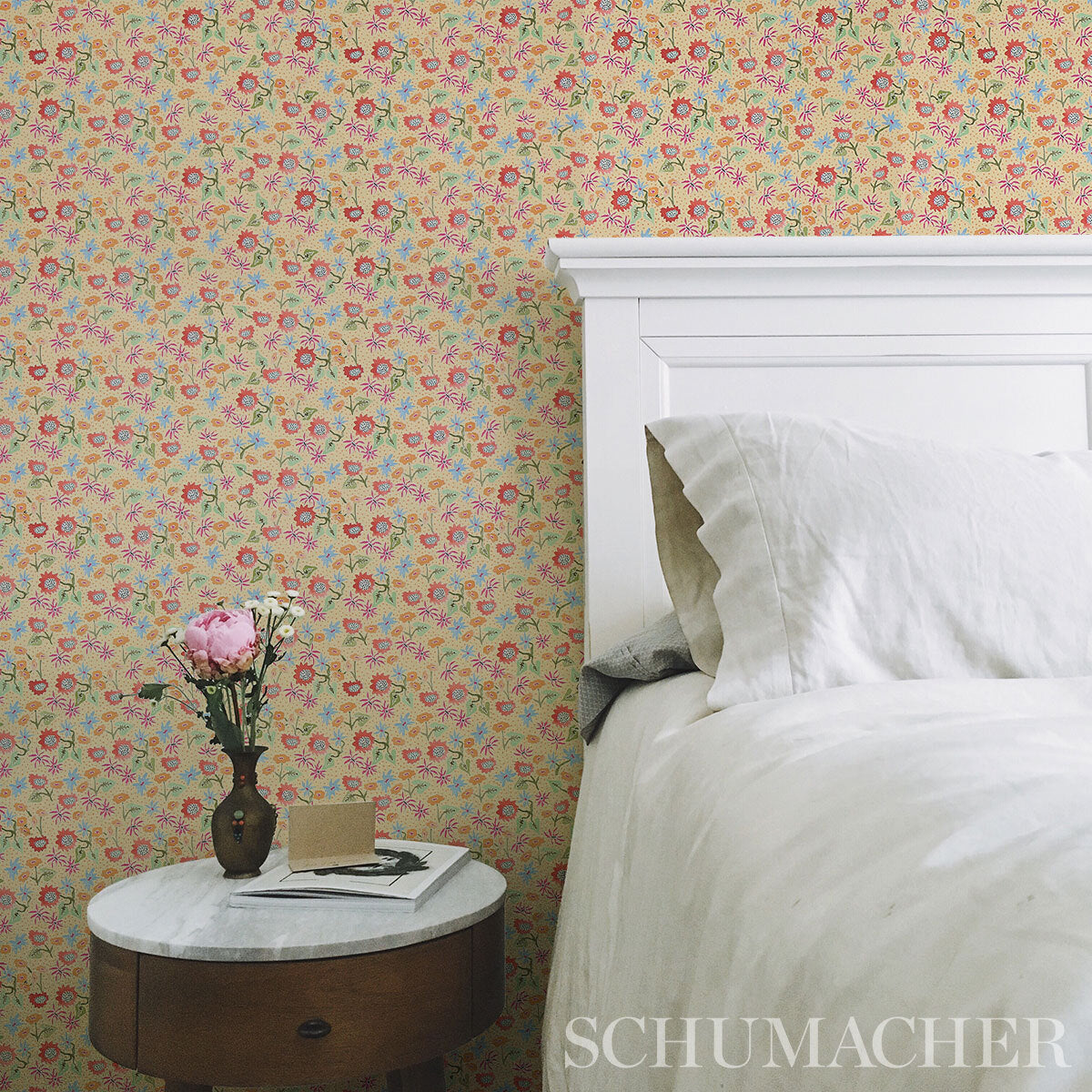 Pastel floral wallpaper with pink, yellow and blue blossoms; a white paneled bed and a round wooden nightstand with a pink vase visible in the room.