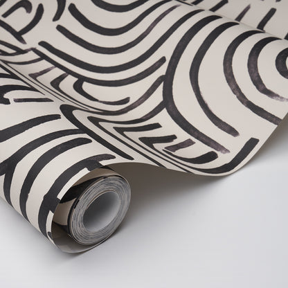 Roll of carbon-colored wallpaper with bold abstract black wavy stripes, partially unrolled.