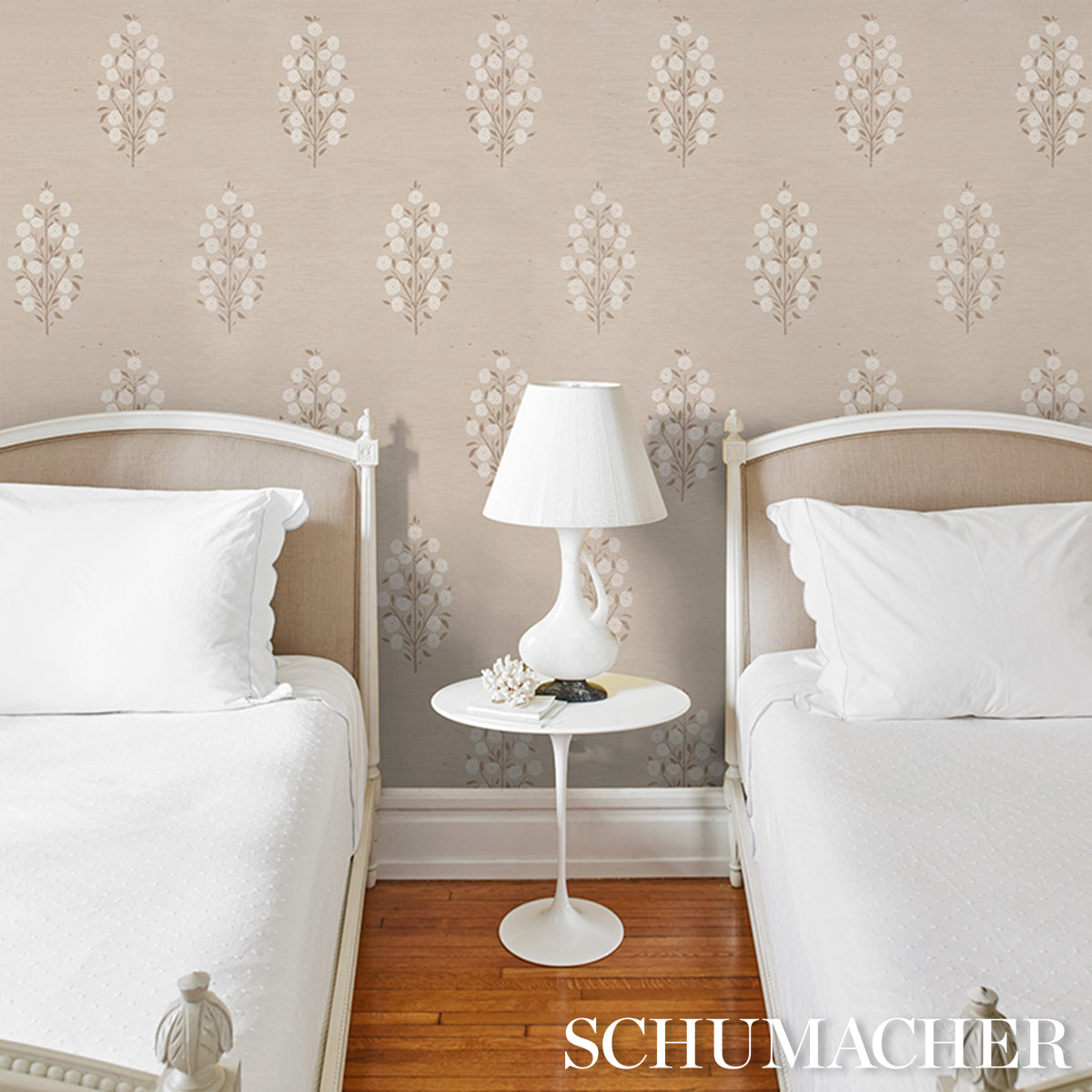 Twin bedroom with white bedding, beige upholstered headboards, round white nightstand, white lamp, floral wallpaper.