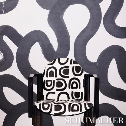 Black wood-arm accent chair with white fabric and bold black geometric pattern, set against a monochrome abstract wall.