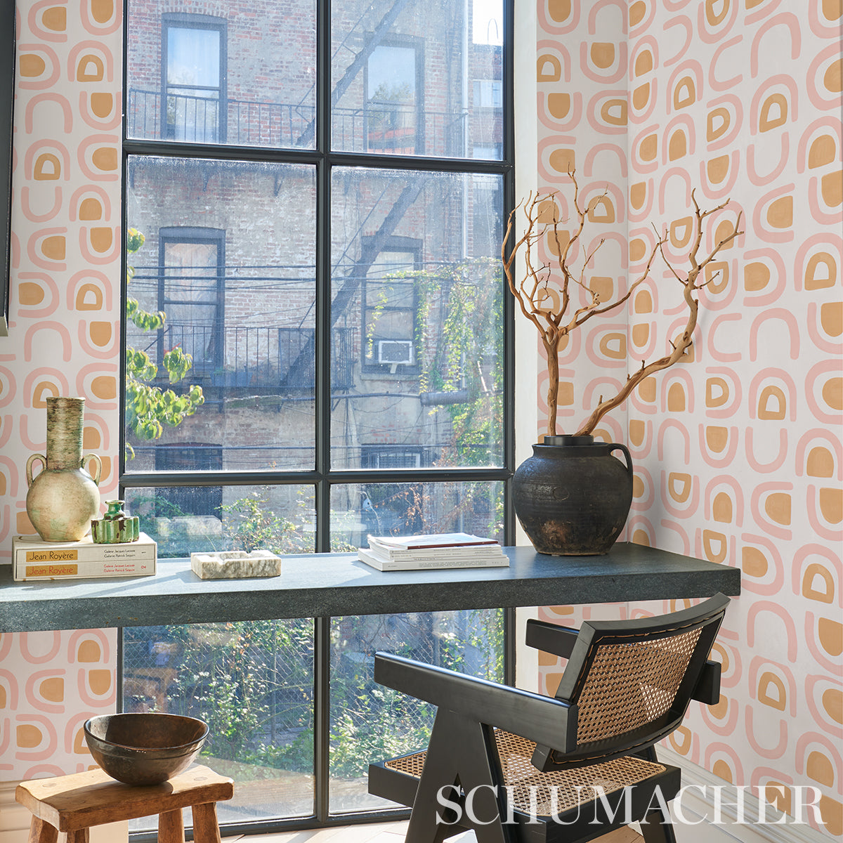Mid-century home office with gray desk, black angular chair with caned back, pink geometric wallpaper, vase with branches.
