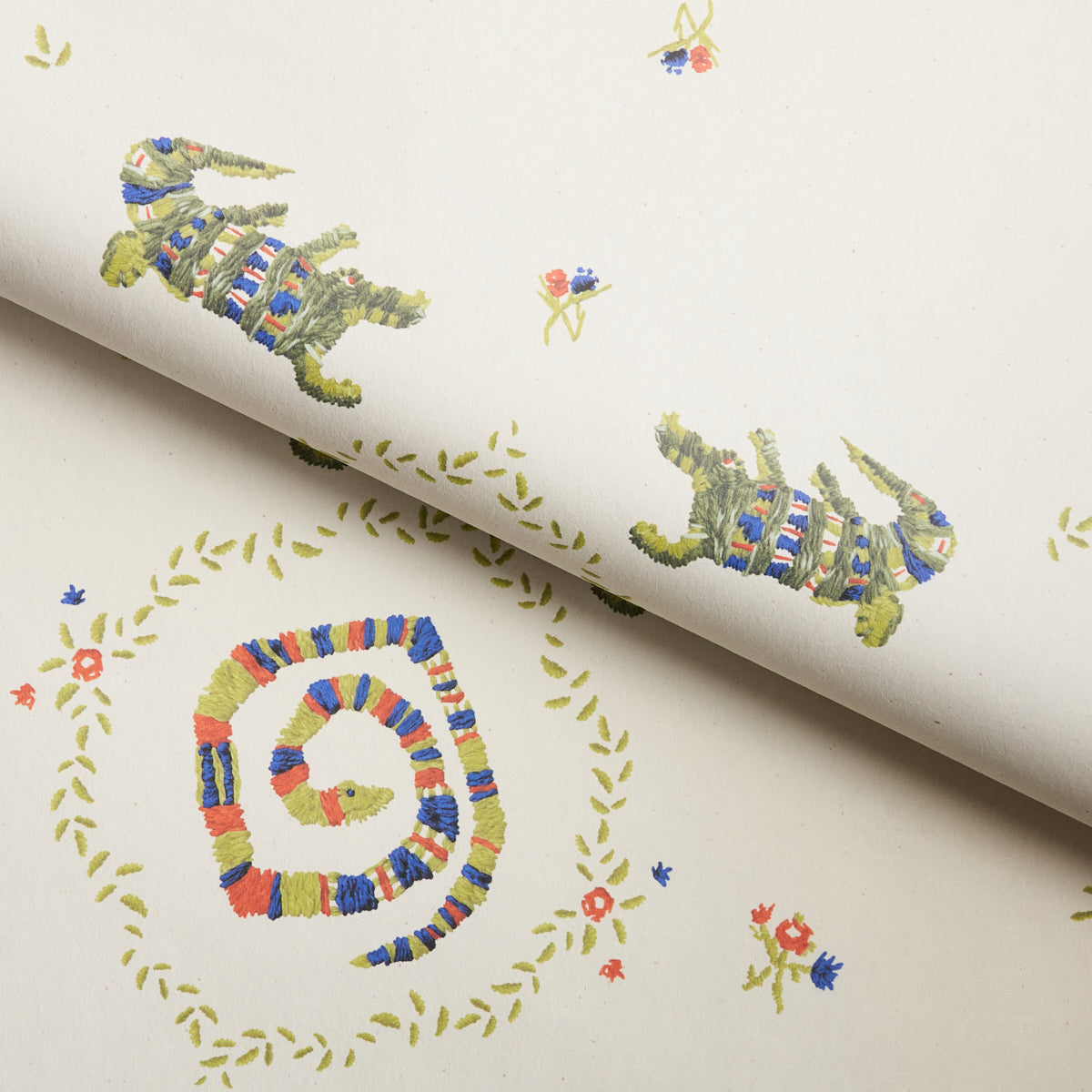 Cream wallpaper with multicolor knitted-look crocodile motifs, circular laurel wreaths, and tiny flowers.