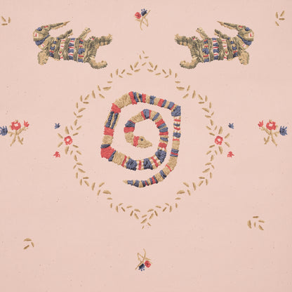 Pastel pink fabric with multicolor yarn embroidery forming a centered spiral, gold leafy border motifs and small florals in folk-art style.