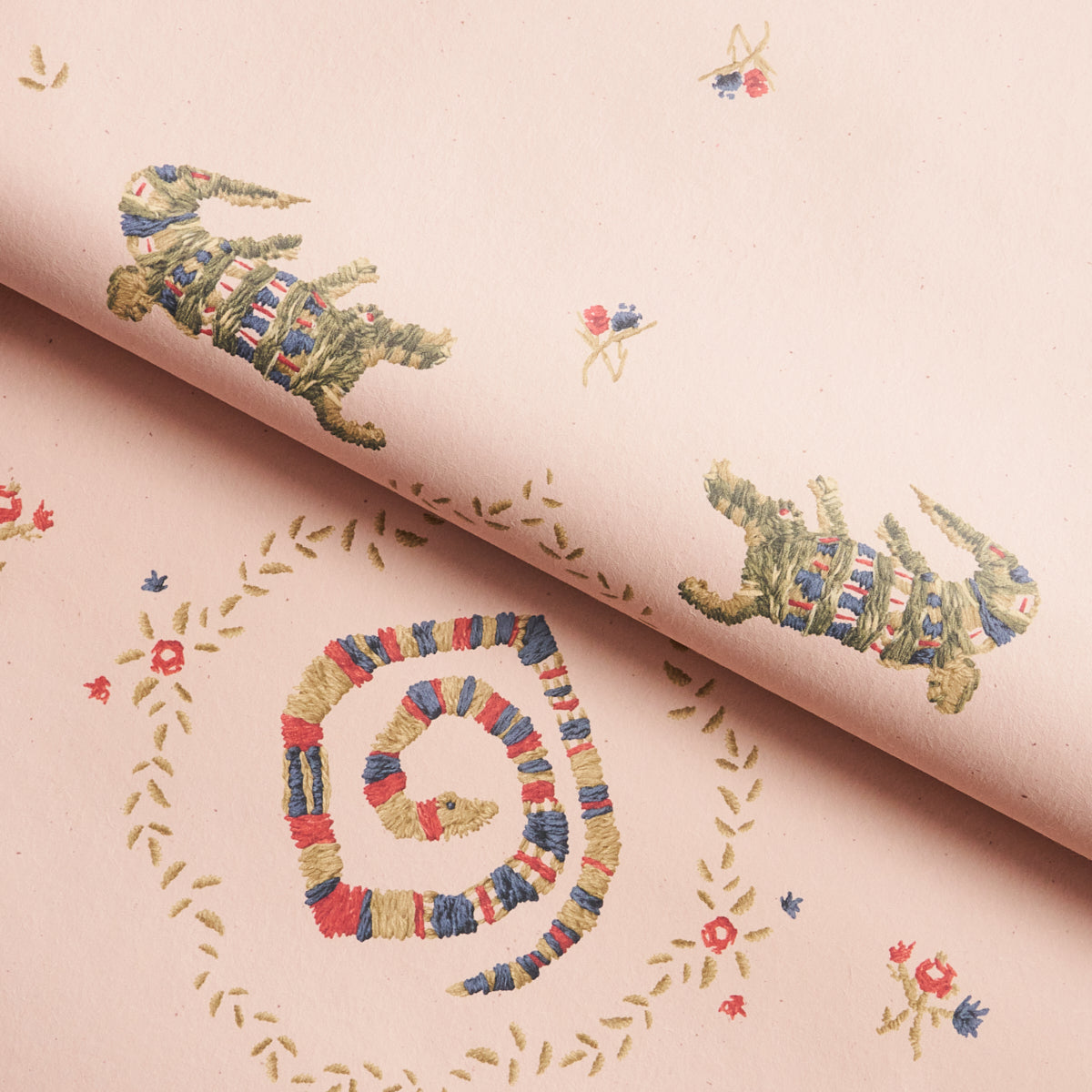 Muted pink backdrop fabric with embroidered-style spirals and small floral motifs in red, blue, and gold.