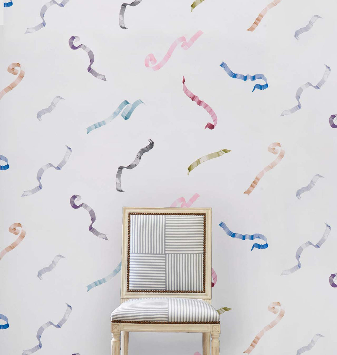 Pastel confetti wallpaper on ivory background with a subtle multi-color pattern; a light wood chair with striped gray and white upholstery partially visible in front of the wallpaper.