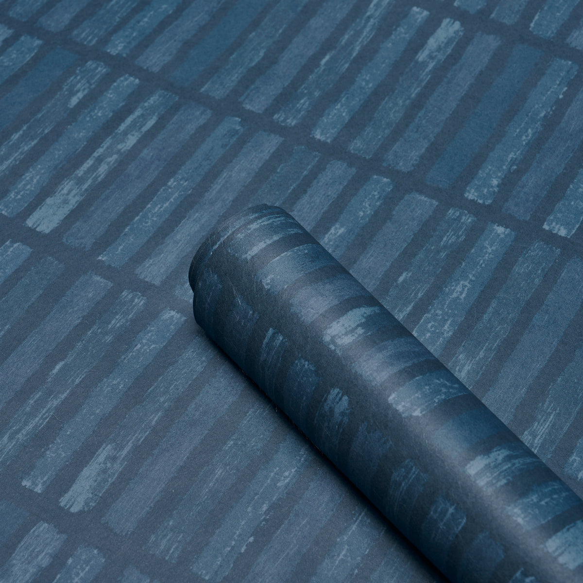 Dark blue rolled fabric swatch on a blue striped surface; matte finish, versatile textile display.