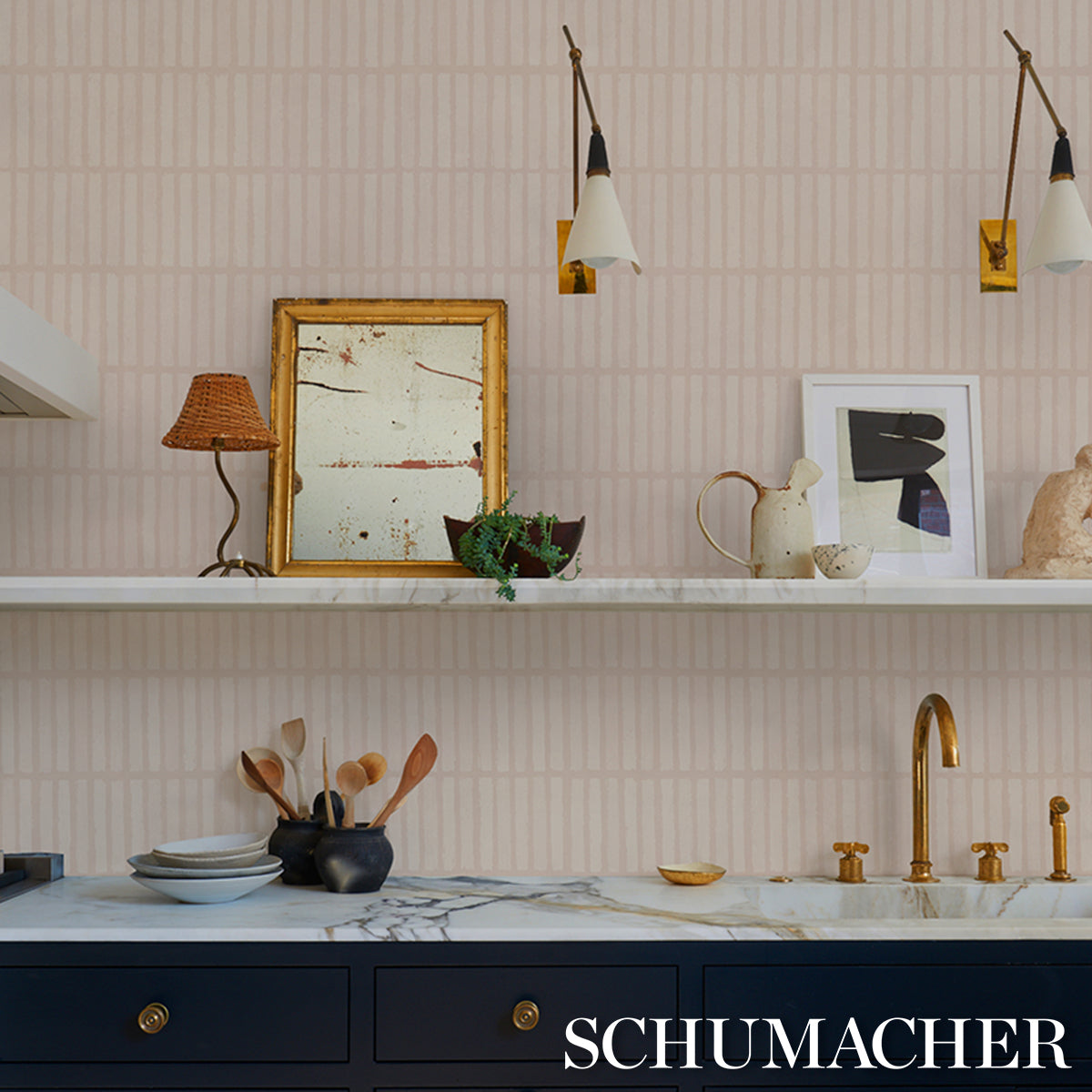 Pink striped wallpaper kitchen with marble countertop, navy cabinets, gold faucet, framed art, teapot and spoons.
