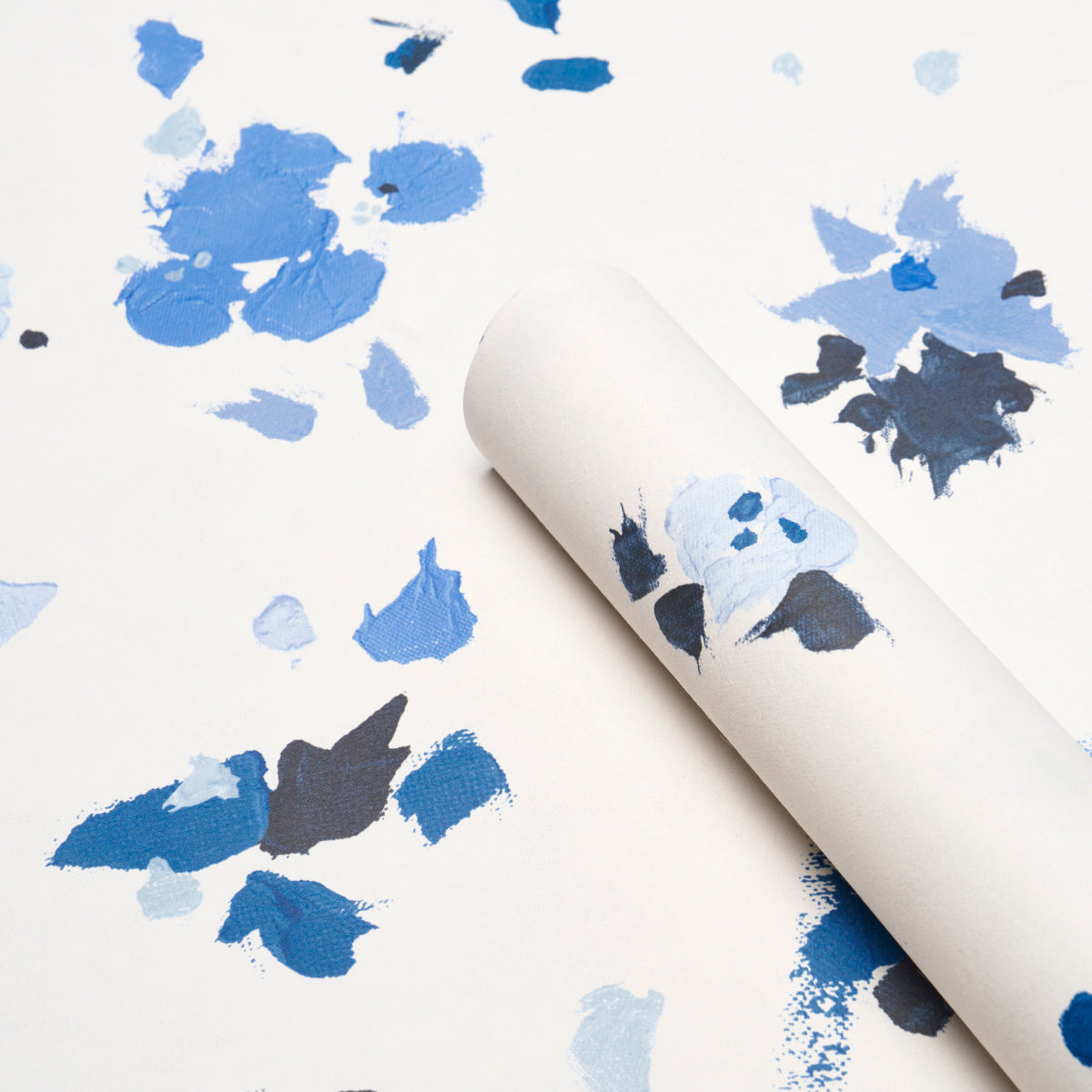 White wallpaper roll with abstract blue paint splatters in navy and light blue, rolled for display.