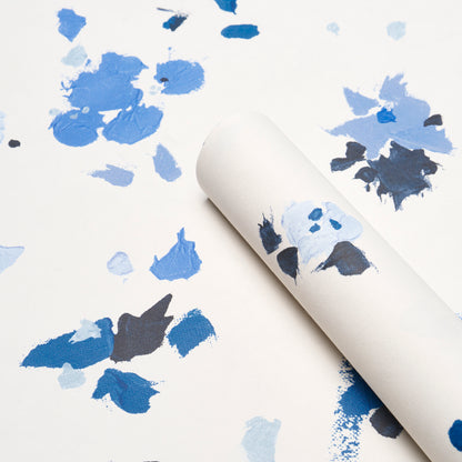 White wallpaper roll with abstract blue paint splatters in navy and light blue, rolled for display.