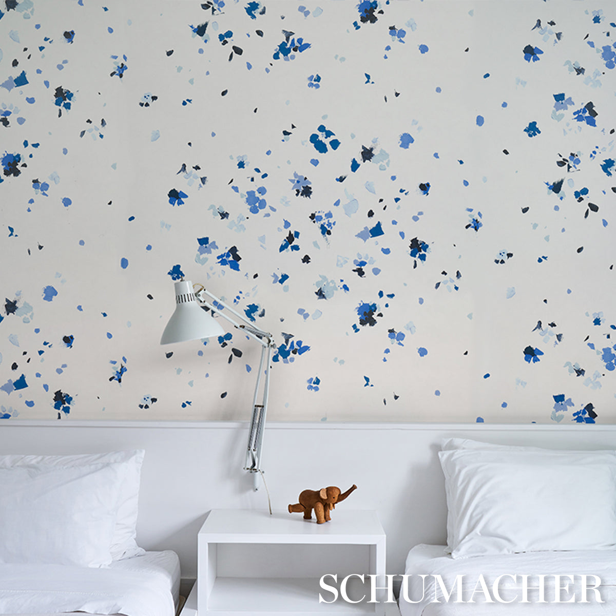 White bedroom with blue floral wallpaper, chrome adjustable wall lamp, and white nightstand with a brown elephant figurine.