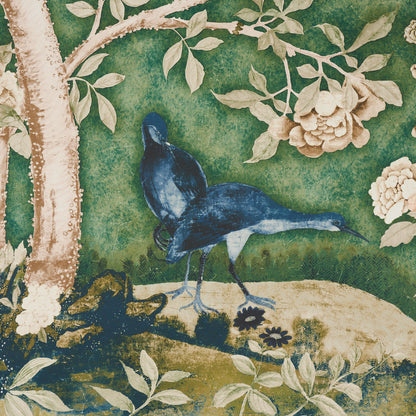 Blue birds with long legs stand on sandy ground amid a green garden scene with white blossoms and a tree trunk.