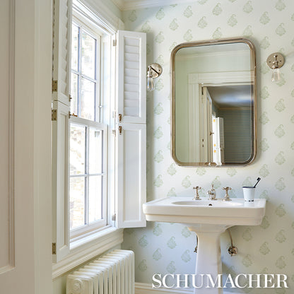 Vintage pedestal sink in a pale green damask bathroom, rounded brass-framed mirror, window with shutters, brass fixtures.