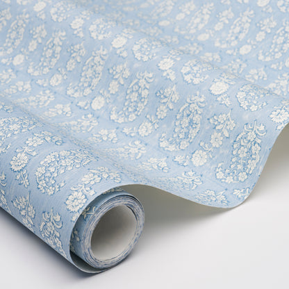 Light blue jacquard fabric with white floral damask pattern, rolled up, ideal for drapery or upholstery.