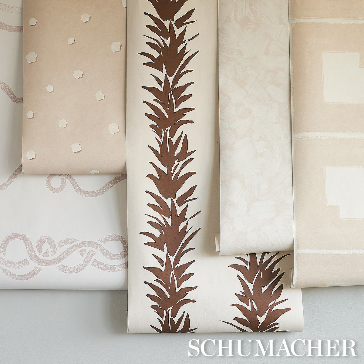 Schumacher wallpaper rolls in beige tones; central brown palm frond pattern with complementary dotted, rope, and geometric designs