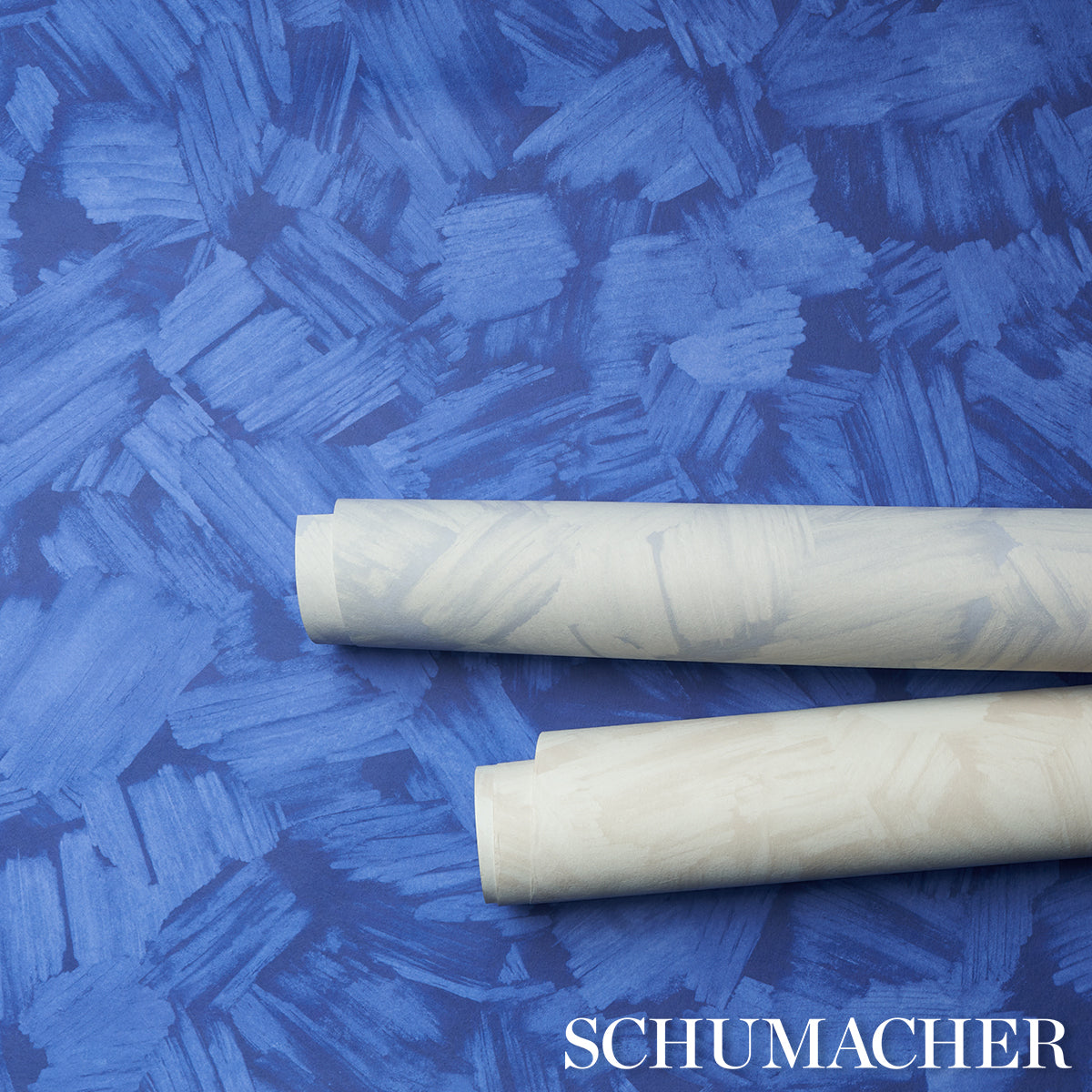 Two white wallpaper rolls lying diagonally on a bright blue textured backdrop.