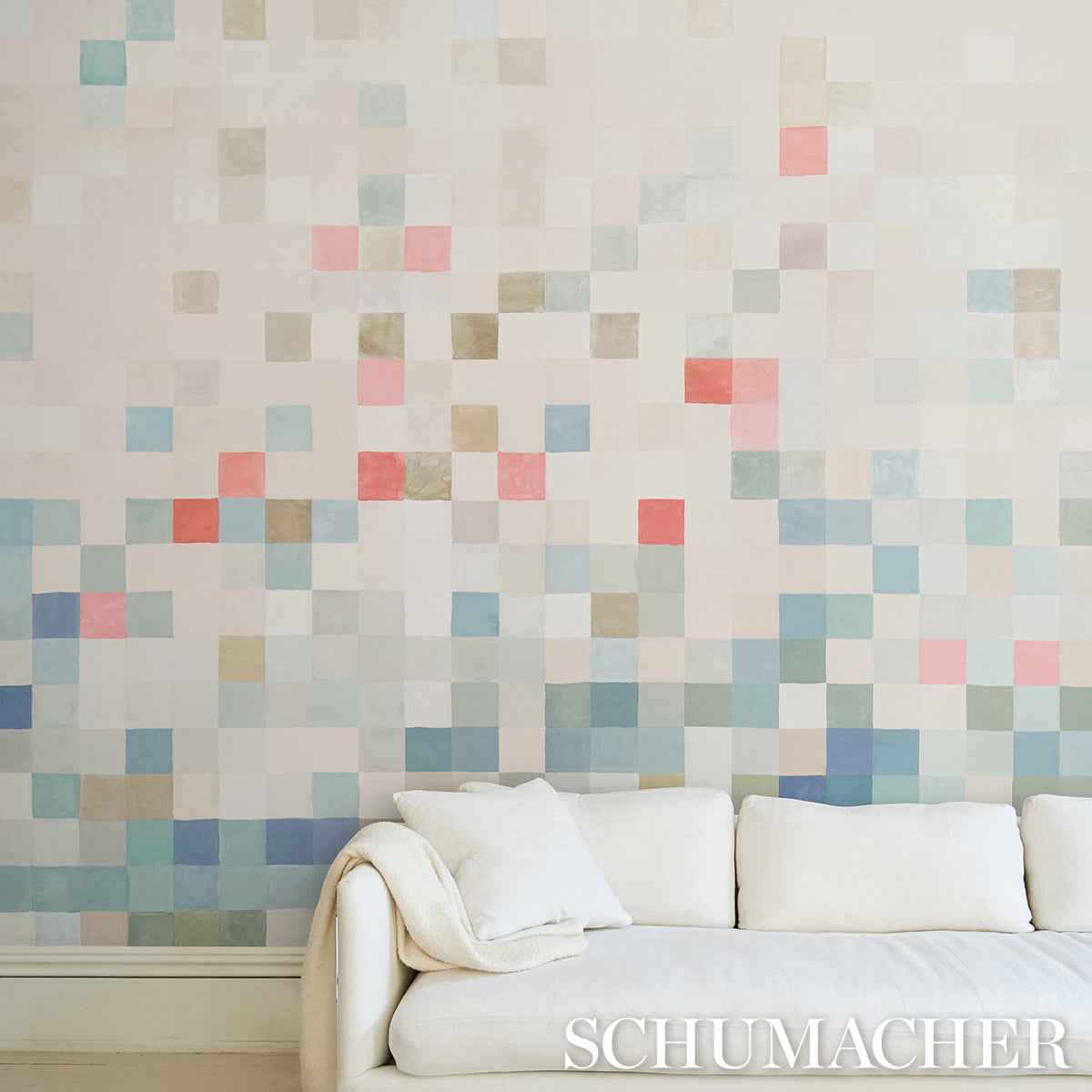 Pastel square mosaic wall mural in blues, pinks & beiges behind a white upholstered sofa with a cream throw.